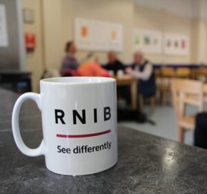 RNIB Scotland Cafe, people faded in the background with a mug at the forefront with RNIB Scotland written on it.